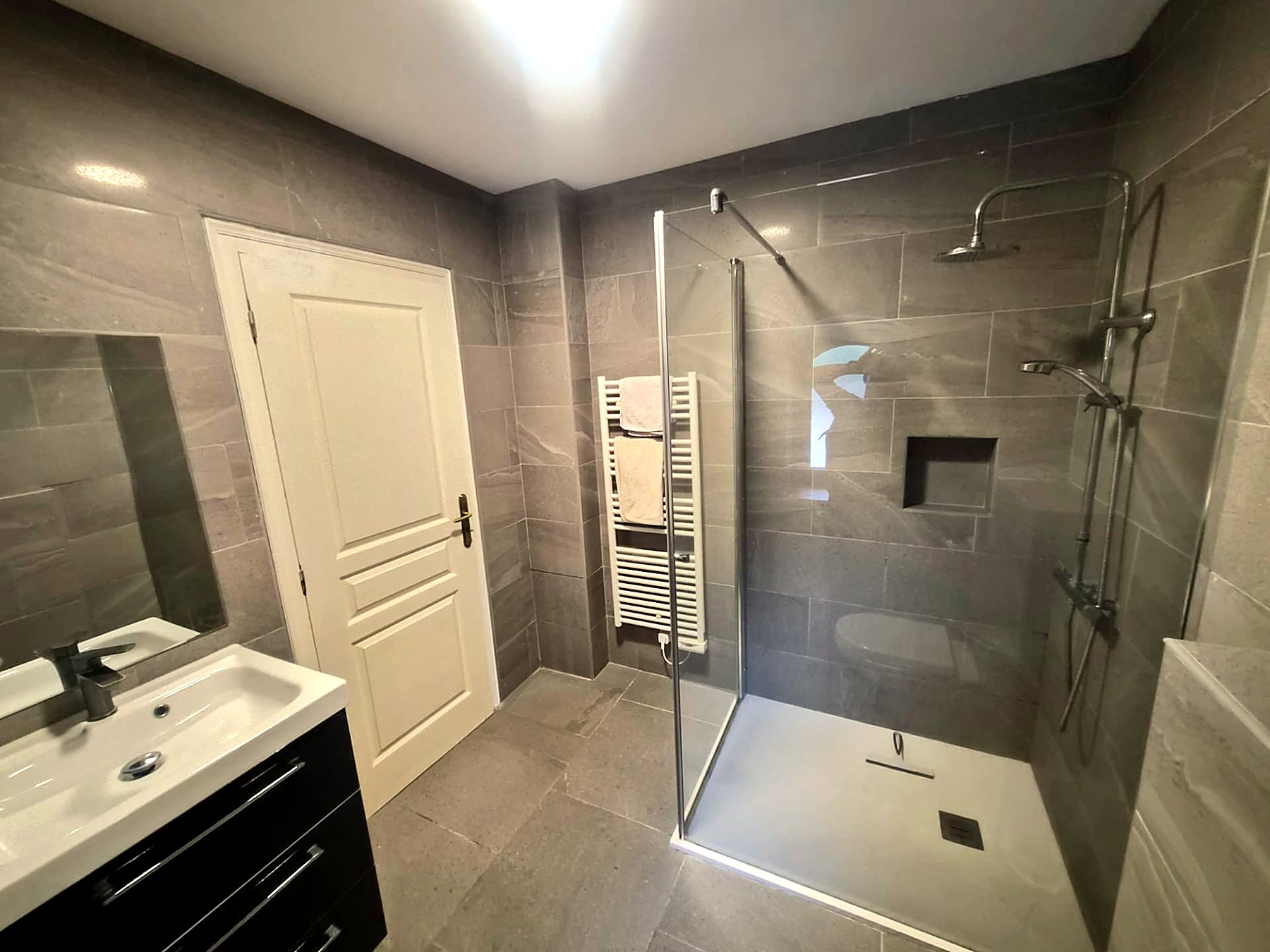 Grey stone-tiled shower room with rainfall shower, basin and WC